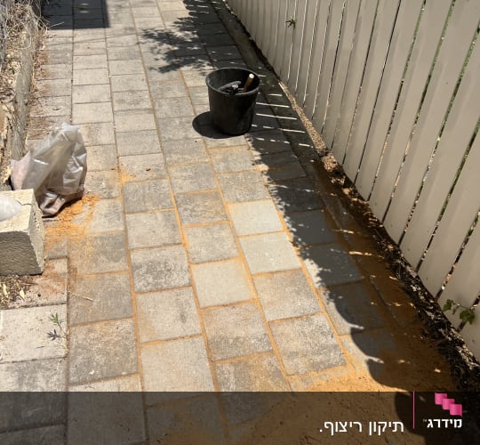 כלי עבודה ודלי על שביל מרוצף עם חול